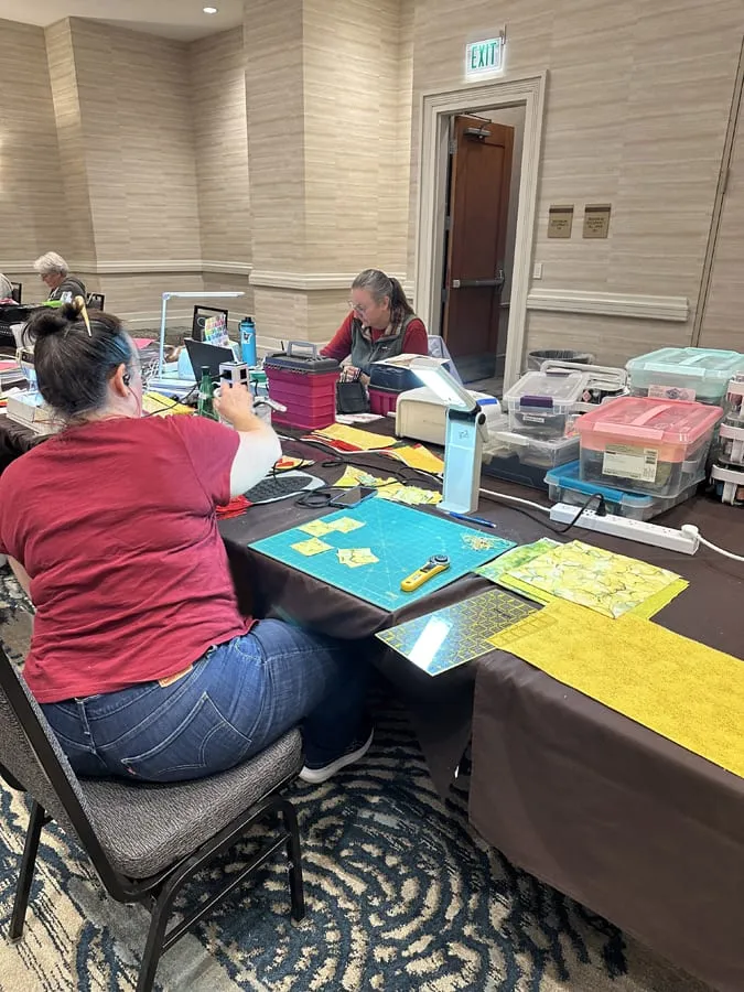 A retreat-goer at her table cutting fabric squares on a cutting mat